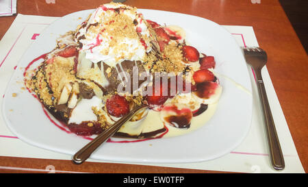 Crepe mit weisser und Milchschokolade mit einer versteckten Kugel Eis, Banane, Erdbeere, geerdeten Nüssen, Sahne und zwei f Stockfoto