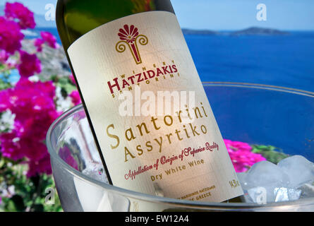 GRIECHISCHER WEIN IM FREIEN Blick auf die sonnenbeschienene Santorini Assyrtiko weiß Weinflasche im Eiskühler mit Bougainvillea und Agean Meer Im Hintergrund Griechenland Stockfoto