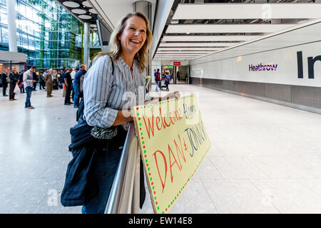 Eine Mutter hält ein Schild willkommen ihrem Sohn und seinem Freund Zuhause Reisen, Flughafen Heathrow, London, England Stockfoto