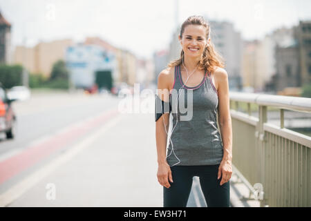 Eine Frau lächelt glücklich, als sie eine Pause auf einer Brücke nimmt. Sie ist entspannt, glücklich und Fit, und genießen Sie das Training in der Sonne Stockfoto