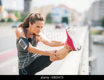 Eine sportliche Frau erstreckt sich vor dem Schlafengehen auf einen langen Lauf. Sie trägt eine Manschette am Arm, die ihr Gerät hält. darauf Stockfoto