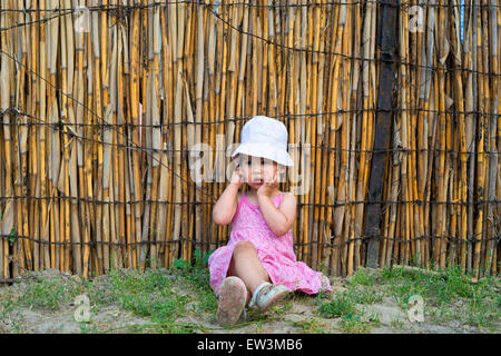 kleines Mädchen ihr den Mund mit Palmen und Blick zur Seite verärgert Stockfoto