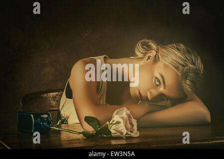 Schöne junge Frau und eine Rose auf dem Tisch Stockfoto