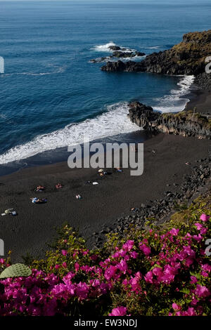 Die Badenden liegen an einem schwarzen Sandstrand vulkanischen Ursprungs am Strand Playa El Bollullo in einer abgeschiedenen Bucht östlich der Stadt Puerto de La Cruz im Norden Teneriffas; eine der kanarischen Inseln des spanischen Archipels vor der Küste Nordwestafrikas. Stockfoto