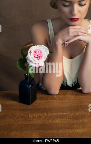 Schöne junge Frau und eine Rose auf dem Tisch Stockfoto