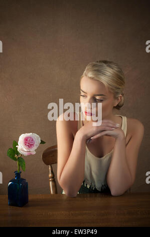 Schöne junge Frau und eine Rose auf dem Tisch Stockfoto