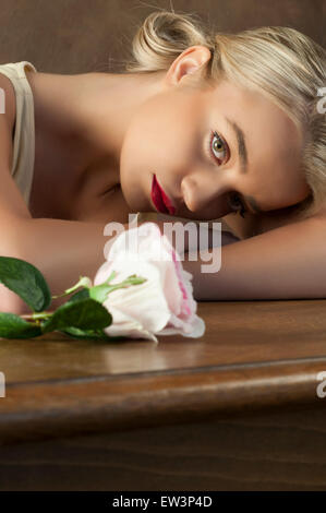 Schöne junge Frau und eine Rose auf dem Tisch Stockfoto
