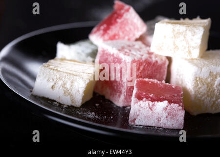 Turkish Delight Stücke auf dunklen Teller auf schwarzem Hintergrund Stockfoto