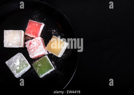 Turkish Delight Stücke auf dunklen Teller auf schwarzem Hintergrund Stockfoto