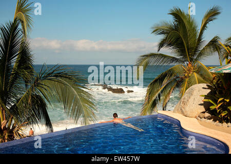 Eine junge Frau liegt am Rande des einen Infinity-Pool mit Blick auf die mexikanische Küste am Strand von Sayulita. Stockfoto