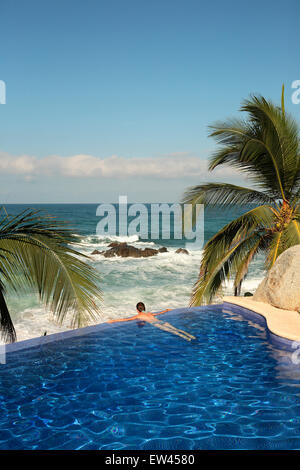 Eine junge Frau liegt am Rande des einen Infinity-Pool mit Blick auf die mexikanische Küste am Strand von Sayulita. Stockfoto