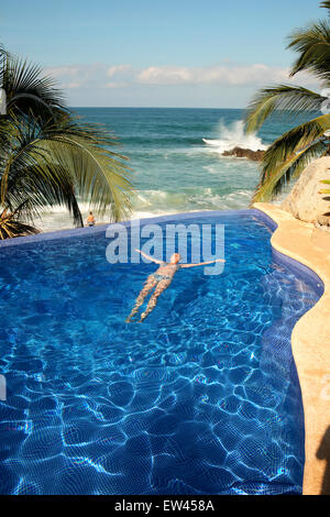 Eine junge Frau liegt am Rande des einen Infinity-Pool mit Blick auf die mexikanische Küste am Strand von Sayulita. Stockfoto