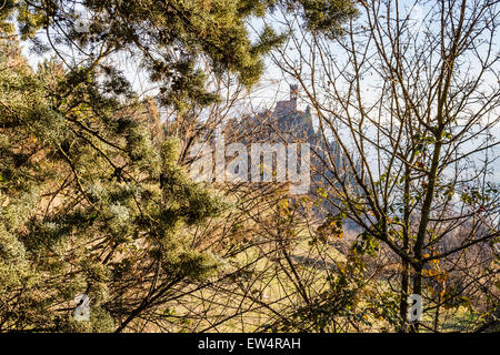 Ein mittelalterlichen Zinnen Uhrturm steht auf einem Gipfel mit Blick auf das Tal eines Dorfes und eines Landes Ackerland, Büschen, Zypressen und andere Bäume unter krabbelt im Nebel von einem sonnigen Wintertag Stockfoto