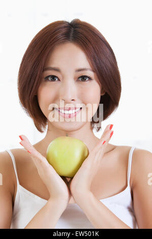 Junge Frau hält einen Apfel und lächelt in die Kamera Stockfoto