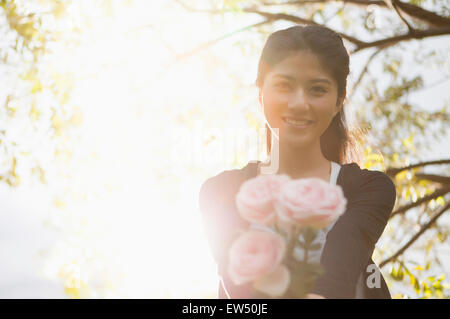 Junge Frau hält einen Blumenstrauß und lächelt in die Kamera Stockfoto