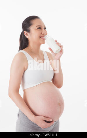 Schwangere Frau trinken eine Flasche Milch und wegschauen mit Lächeln, Stockfoto