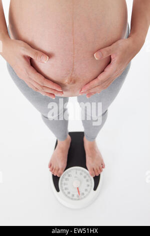 Schwangere Frau mit den Händen auf den Bauch auf der Waage stehen, Stockfoto