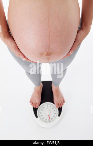 Schwangere Frau mit den Händen auf den Bauch auf der Waage stehen, Stockfoto