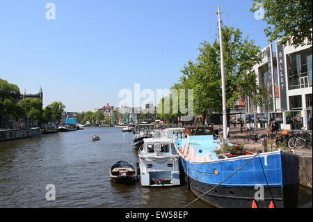 Festgemachten Boote am Fluss Amstel in Amsterdam, Niederlande, neben Stopera Gebäude (Rathaus) auf der rechten Seite Stockfoto