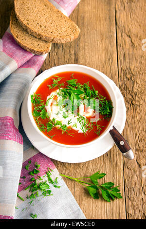 Hausgemachte kalte Tomatensuppe mit Frischkäse und frischen Kräutern auf rustikalen Holztisch Stockfoto