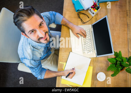 Lässige Geschäftsmann Notizen in seinem Notizblock und lächelt in die Kamera Stockfoto