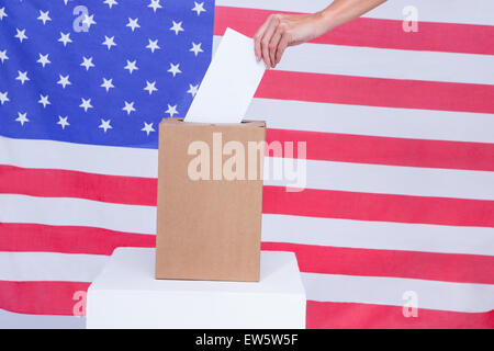 Hand, die Stimmzettel in Abstimmung Kästchen hinter amerikanische Flagge setzen Stockfoto