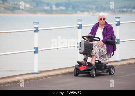 Frau Reiten Elektromobil entlang am Meer am Strand von Weymouth, Dorset im Juni Stockfoto