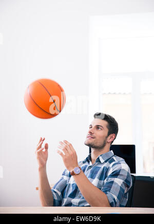 Glücklich Kaufmann am Tisch sitzen und wirft Ball im Büro Stockfoto