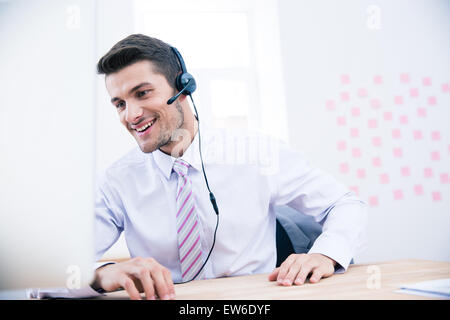Porträt eines lächelnden männlichen Betreiber mit Kopfhörer sitzt am Tisch im Büro Stockfoto