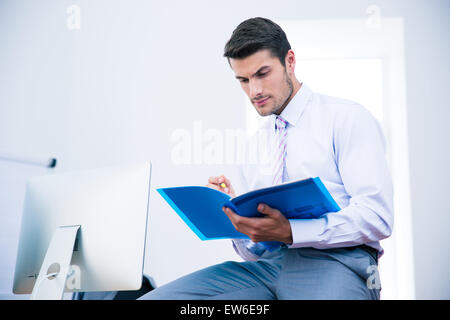 Geschäftsmann auf dem Tisch sitzen und lesen Dokument im Büro Stockfoto