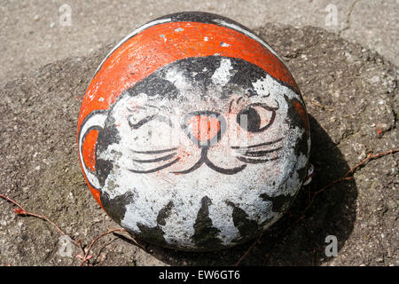 Japan, Onomichi. Runder Stein mit dem Gesicht einer Katzenkwinkerei, auf dem Boden vor dem Restaurant, Schild für Treffpunkt für die Begrüßung der Kunden. Stockfoto