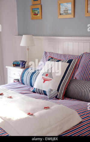 Appliziert und gestreiften Kissen mit einem Seethema auf Bett mit einer gefalteten weißen Decke in einem Ferienhaus Schlafzimmer Stockfoto