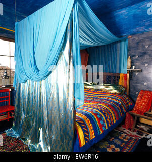 Türkis und satin Vorhänge am Baldachin über dem Bett mit bunten Patchwork quilt in Blau der neunziger Jahre Schlafzimmer Stockfoto