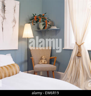 Fünfziger Jahre gestreift blau Stuhl und Lampe in der Ecke des neunziger Jahre Schlafzimmer mit weißen Vorhänge am Fenster Stockfoto