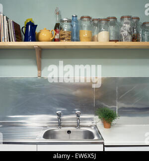 Reihe von Glas Vorratsdosen auf hölzernen Regal über Edelstahl Waschbecken in Wirtschaft Küche Stockfoto