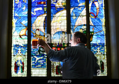 Ein Mann, einen Pint Bier vor einem Buntglas-Fenster heben. Bild: Scott Bairstow/Alamy Stockfoto