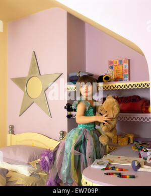 Kleine Mädchen tragen eine Fee Kostüm hält einen Teddybär, stehend in einem Sterne themed Schlafzimmer Stockfoto