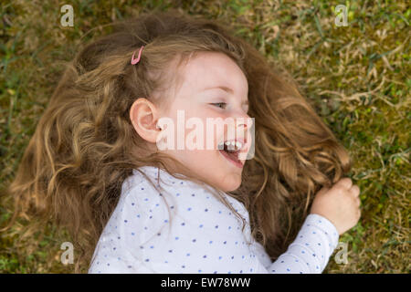 Kleines Mädchen auf einer Wiese liegend lachen Stockfoto