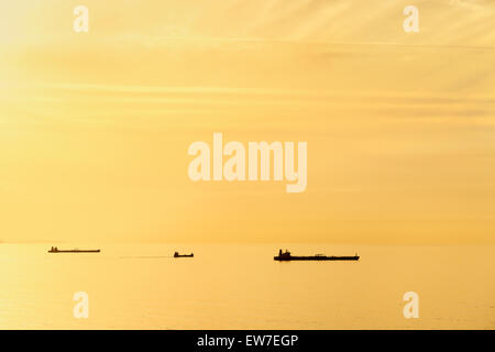 drei Frachtschiffe bei Sonnenuntergang mit ruhiger See Stockfoto
