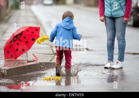 Kleiner Junge mit Regenschirm, in schlammigen Pfützen springen Stockfoto