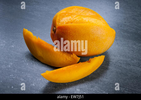 Frisch geschnittene Mango-Frucht mit Scheiben auf grauem Stein Hintergrund Stockfoto