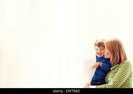 Mutter steht an einem Fenster und küsst ihren Sohn Stockfoto