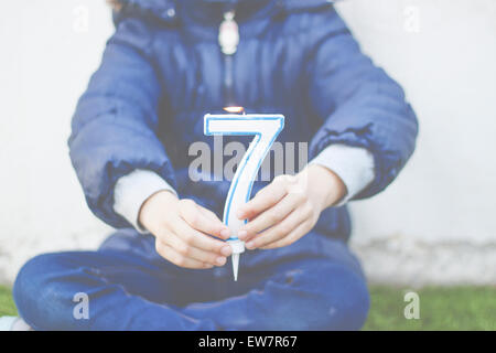 Mädchen sitzen cross legged mit einer Nummer sieben Kerze Stockfoto