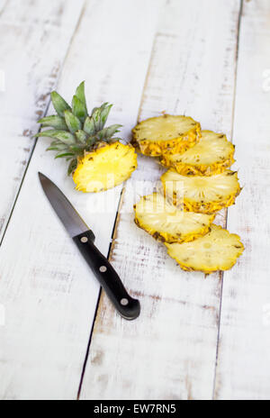 Stillleben mit einer Ananas in Stücke geschnitten, mit einem Messer auf einem Holztisch Stockfoto