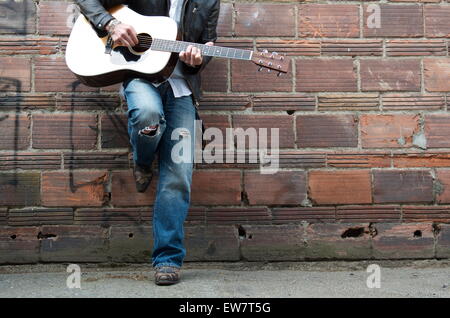 Mann in Lederjacke und Cowboy-Stiefel, die Gitarre zu spielen, in einer Gasse Stockfoto