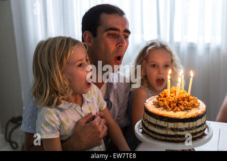 Vater mit seinen beiden Töchtern Ausblasen der Kerzen auf der Geburtstagstorte Stockfoto