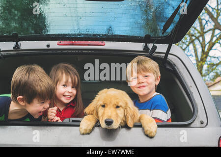 Drei Kinder sitzen im Kofferraum eines Autos mit ihrem neuen Welpen, USA Stockfoto