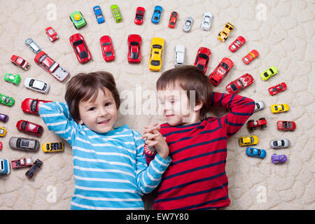 Entzückende jungen, liegend auf dem Boden, Spielzeugautos herum, schaut in die Kamera lachen, geschossen von oben Stockfoto