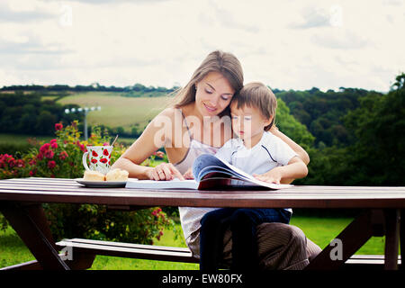 Mutter und Sohn, ein Buch im Freien, Sommertag, süßes Gebäck Essen Stockfoto