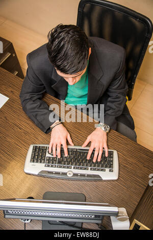 Junger Geschäftsmann sitzt an seinem Schreibtisch tragen Business-Anzug mit Computer, gesehen von oben Perspektive Stockfoto